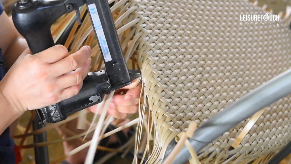 A worker is repairing loose rattan ends with a custom stapler at a workshop.